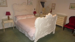 A bedroom with a white ornate bed, a red chair, a dresser, and a nightstand with a lamp. - Tranquil country cottage set in the heart of a traditional family farm. (tenbury wells)