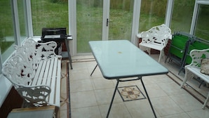 A conservatory with a table and chairs, a piano, and a green bin. - Tranquil country cottage set in the heart of a traditional family farm. (tenbury wells)
