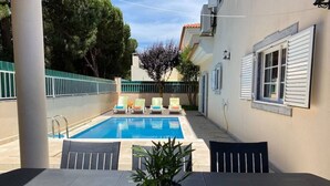 A poolside area with a table and chairs, a potted plant, and a view of a swimming pool. - Lagoa Albufeira House - with private swimming pool (Sesimbra)
