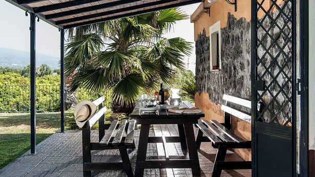 An outdoor patio with a wooden table and benches, surrounded by a garden with palm trees. - Country-house with pool and Etna and sea views (Acireale)