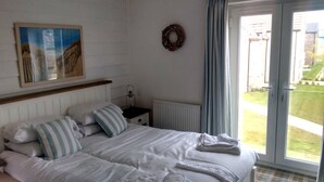 Une chambre à coucher avec un lit, une table de chevet, un radiateur, une fenêtre avec des rideaux et un tableau au mur.