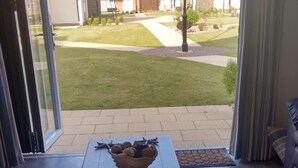 Une pièce avec une table et un saladier de fruits, une porte-fenêtre coulissante donnant sur un jardin, et une vue sur un quartier résidentiel.