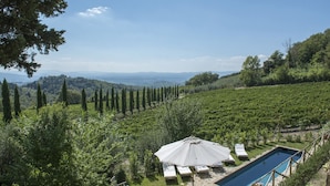 Un espace piscine agrémenté de chaises longues et d’un parasol, entouré d’un vignoble et de cyprès.