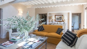 Un salon avec un canapé, une table basse avec des livres, un vase avec des plantes et un escalier.