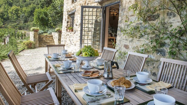 Un espace de restauration extérieur rustique, avec des murs en pierre, des meubles en bois et une table dressée pour le petit-déjeuner.