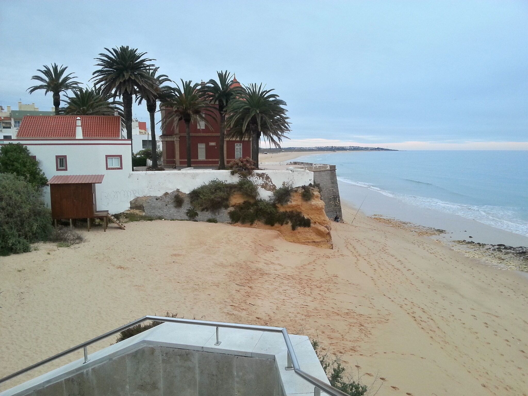 A beachside property with a white building, red roof, and palm trees.