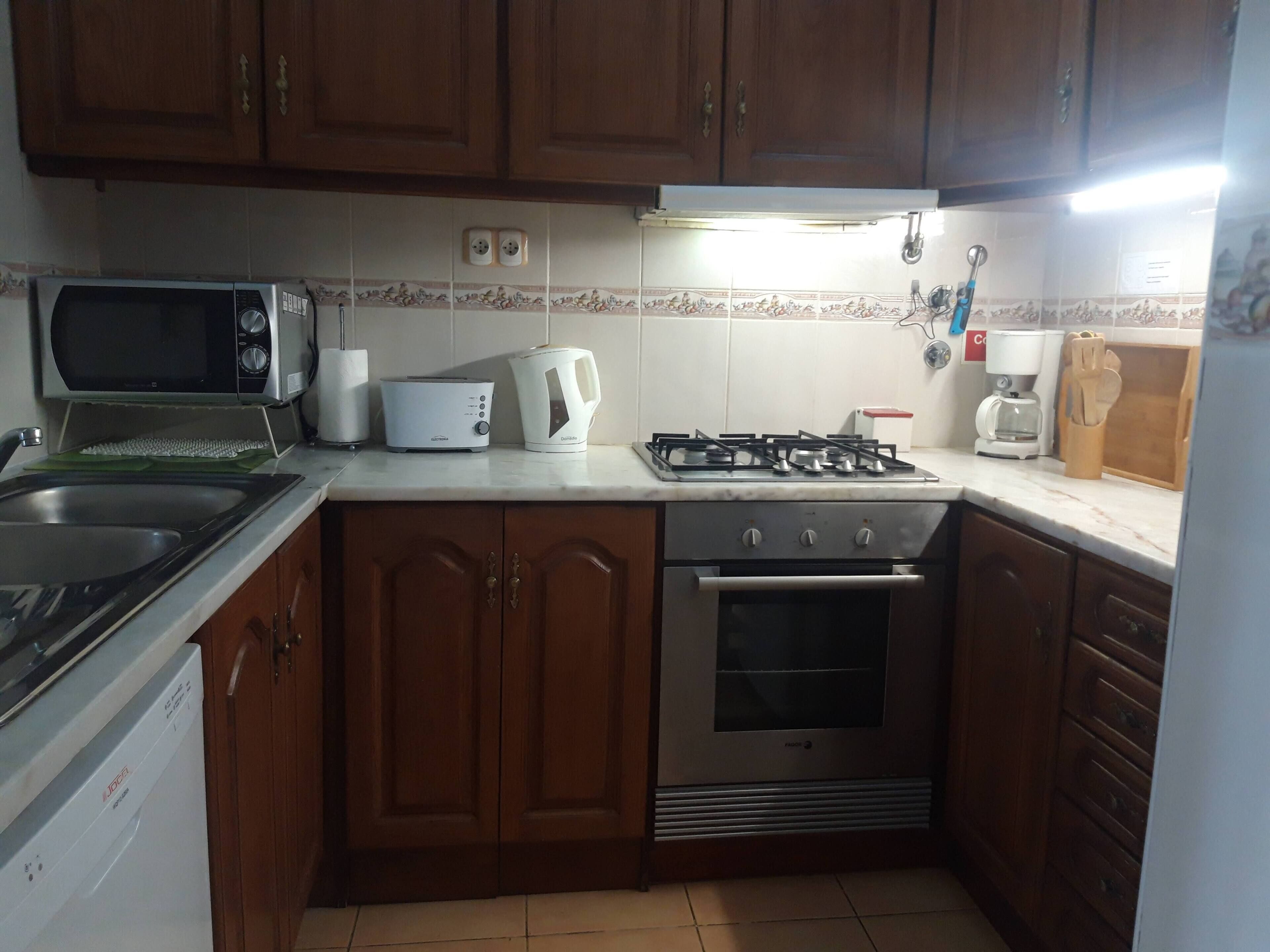 A kitchen with wooden cabinets, a microwave, a toaster, a kettle, a gas stove, and an oven.