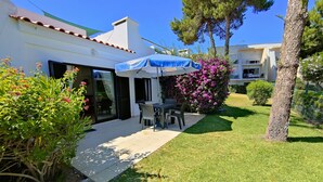A patio area with a table and chairs, a covered umbrella, and a garden with flowering plants. - Tourist Set Alporchinhos (Armação de Pêra - Algarve)