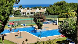 A swimming pool with a view of the sea, surrounded by greenery and a tennis court. - Tourist Set Alporchinhos (Armação de Pêra - Algarve)