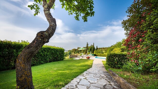 A stone pathway leading to a pool area surrounded by lush greenery and a clear sky.