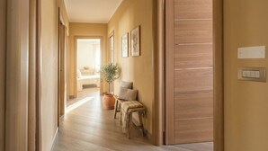 Un couloir avec un plancher en bois, un banc, une plante en pot et une porte avec un interrupteur.