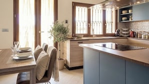 Une cuisine moderne avec un îlot central, un coin repas avec une table dressée pour quatre personnes et une plante en pot.