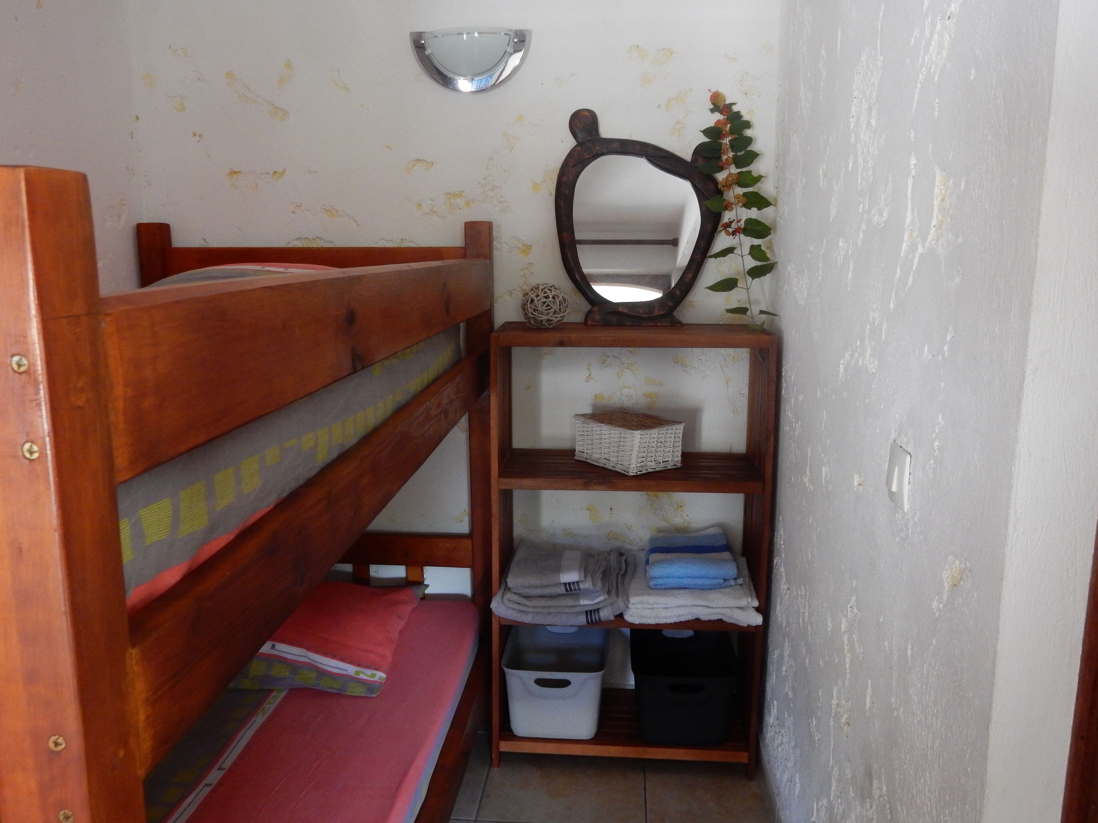 A small, compact room with a bunk bed, a wooden shelf with storage bins, and a wall-mounted mirror.