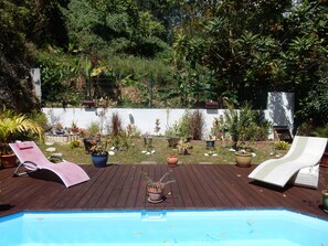 A wooden deck with a pool, surrounded by potted plants and a white wall. - Your holiday in a beautiful area with pool and spa (GOSIER)
