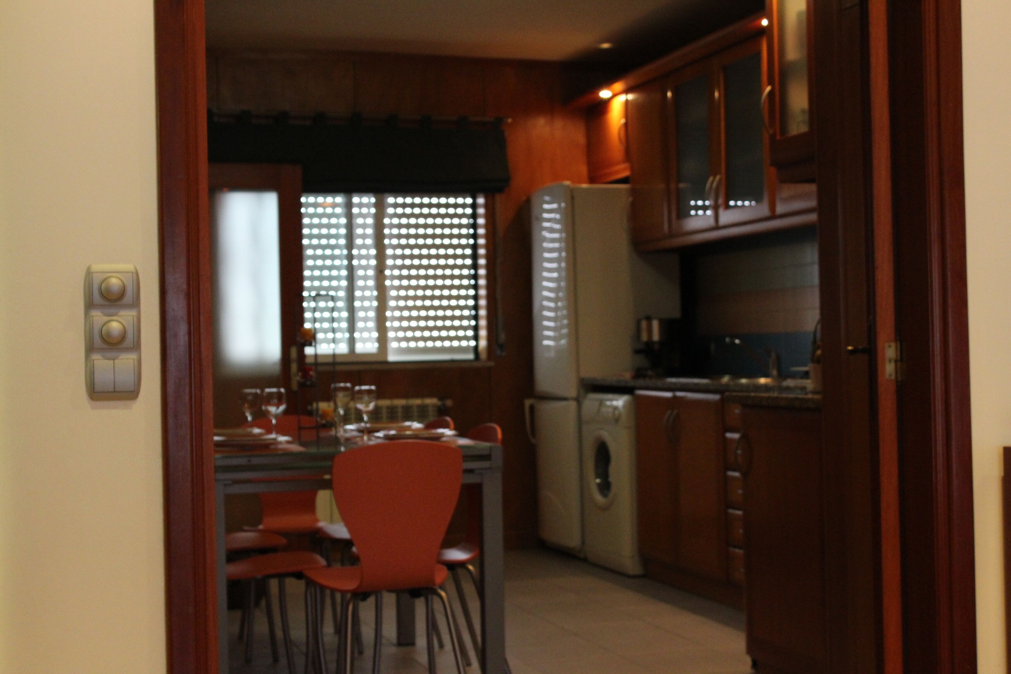 Una cocina con armarios de madera, un refrigerador, una lavadora y una mesa de comedor con sillas.