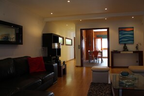 A modern living room with a leather sofa, a glass coffee table, and a dining area in the background. -  Nazare - 3-bedroom apartment, 50 meters from the beach! FREE WIFI  (Nazaré)