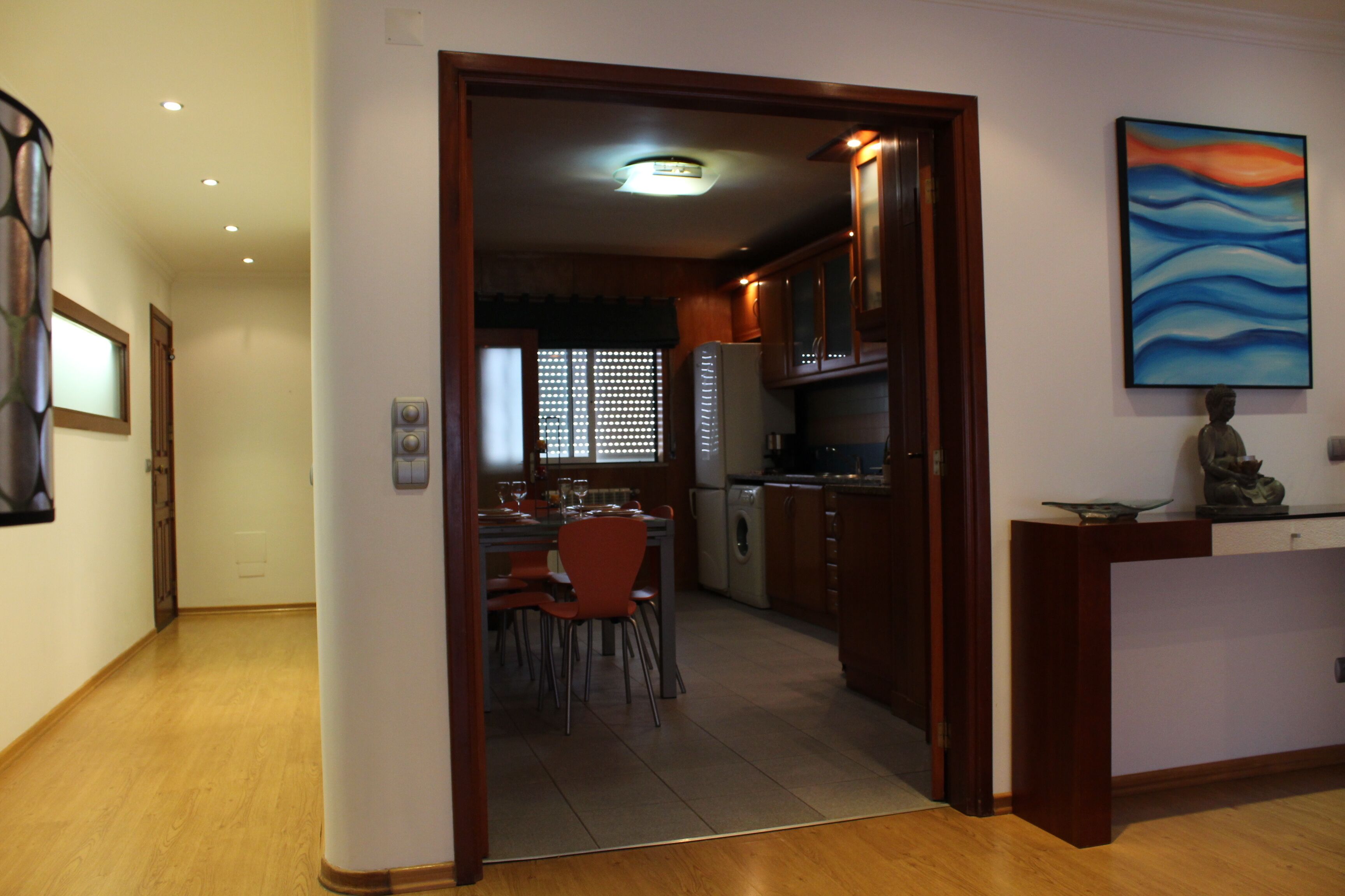 Una cocina moderna con armarios de madera, una zona de comedor con sillas rojas y un cuadro en la pared.