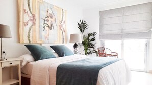 Een slaapkamer met een bed, nachtkastjes, een lamp, een plant en een raam met uitzicht.