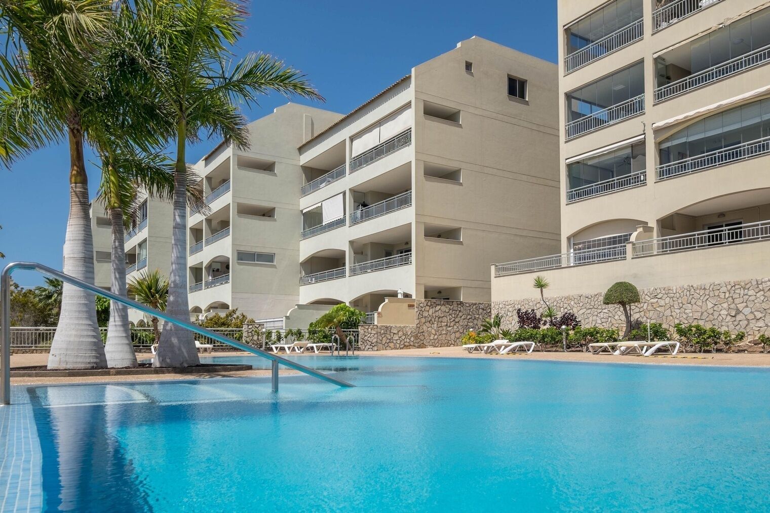 Un hotel con piscina, palmeras y un muro de piedra.