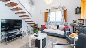Ein modernes Wohnzimmer mit Flachbildfernseher, Couchtisch, Sofa, einer Wendeltreppe mit Holzregalen und einer Kristallleuchter.