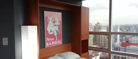 Habitación de hotel con una cama grande, una mesita de noche, una lámpara de pared y un cartel con la imagen de una mujer y el texto "Pates BARONI".
