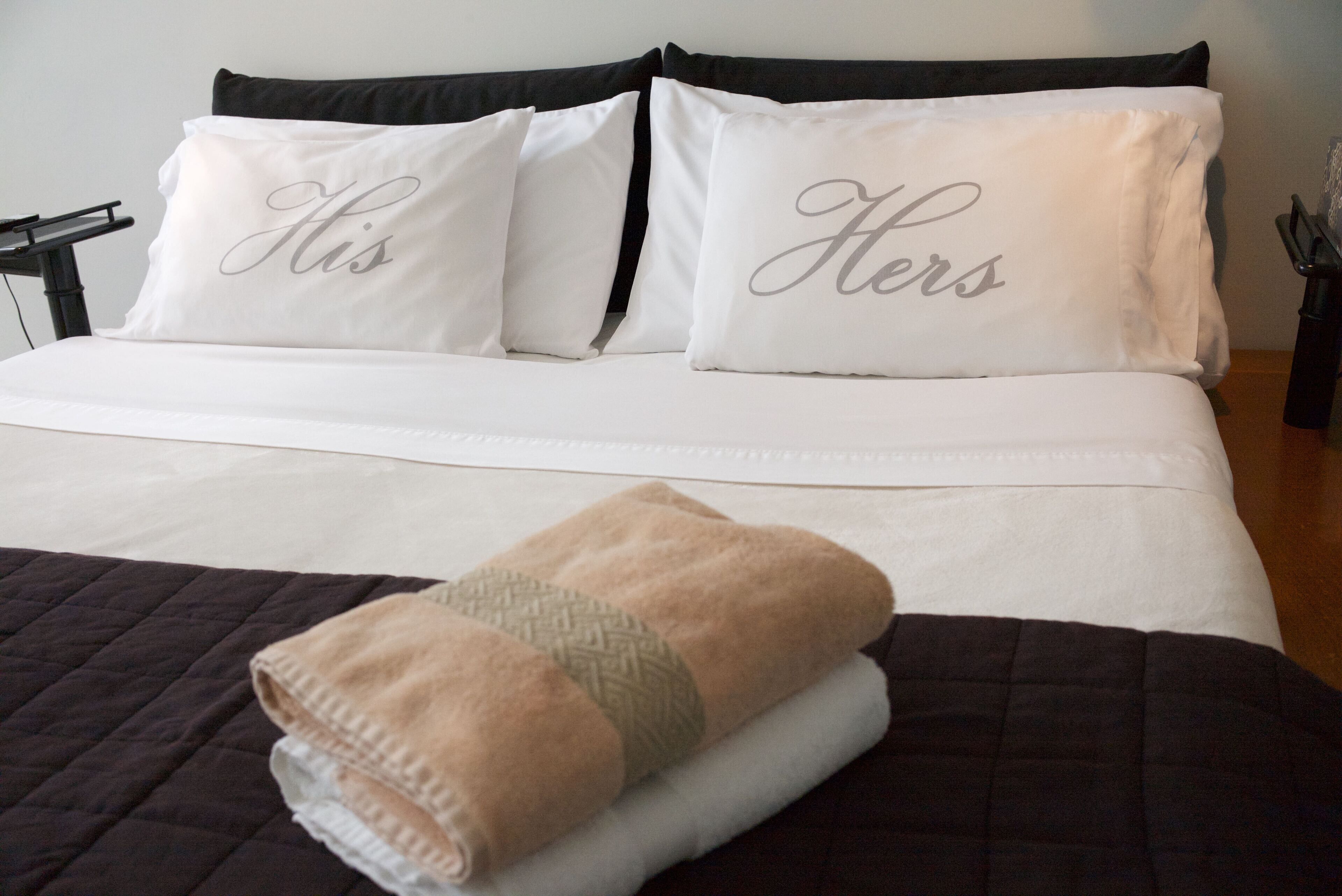 A bed with white bedding and two pillows with the words "His" and "Hers" on them.