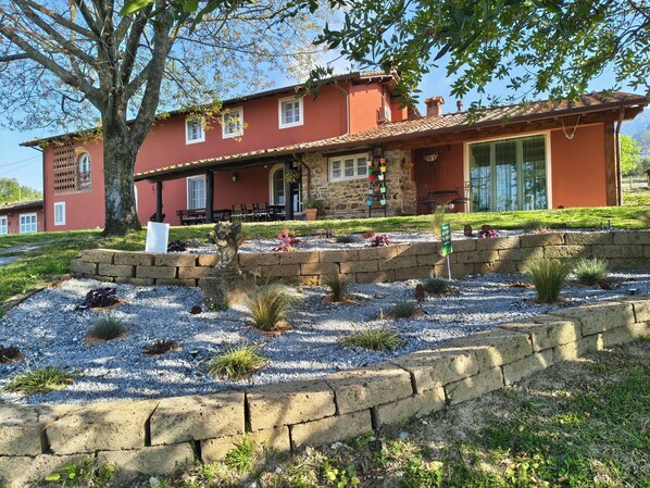 A red building with a stone facade, a covered porch, and a garden with gravel and plants.