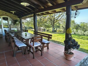 An outdoor patio with a wooden table and benches, surrounded by a stone wall and potted plants.