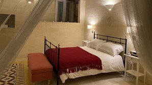 A bedroom with a bed, a nightstand, a bench, a window with curtains, and a wall with a textured pattern.