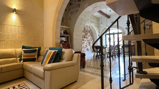 A spacious living area with a beige sofa, patterned rug, and a staircase leading to an upper level.