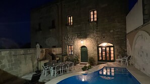 A nighttime view of a pool area with stone walls, a pool, and outdoor seating.