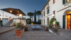 Eine Terrasse im Freien mit einem Tischtennis-Tisch, Blumentöpfen und einer überdachten Sitzgelegenheit mit einer Treppe, die zu einer oberen Ebene führt.