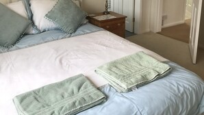 A neatly made bed with a white headboard, blue and grey pillows, and a green towel. There is a wooden nightstand with a lamp and a framed botanical print on the wall. - Spacious House 3 ensuite bedrooms, sleeps 6, Centre of Helmsley, Pet friendly,  (Helmsley)