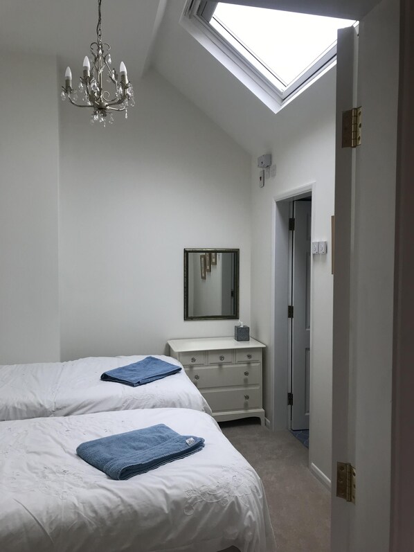 A bedroom with two beds, a dresser, a mirror, and a chandelier.