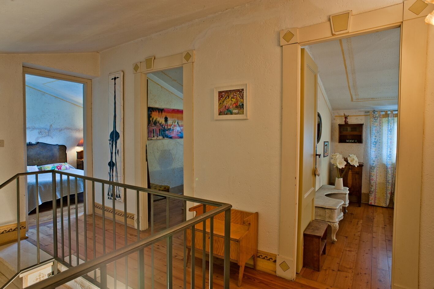 A spacious hallway with a wooden floor, a staircase, and a bed in the background.
