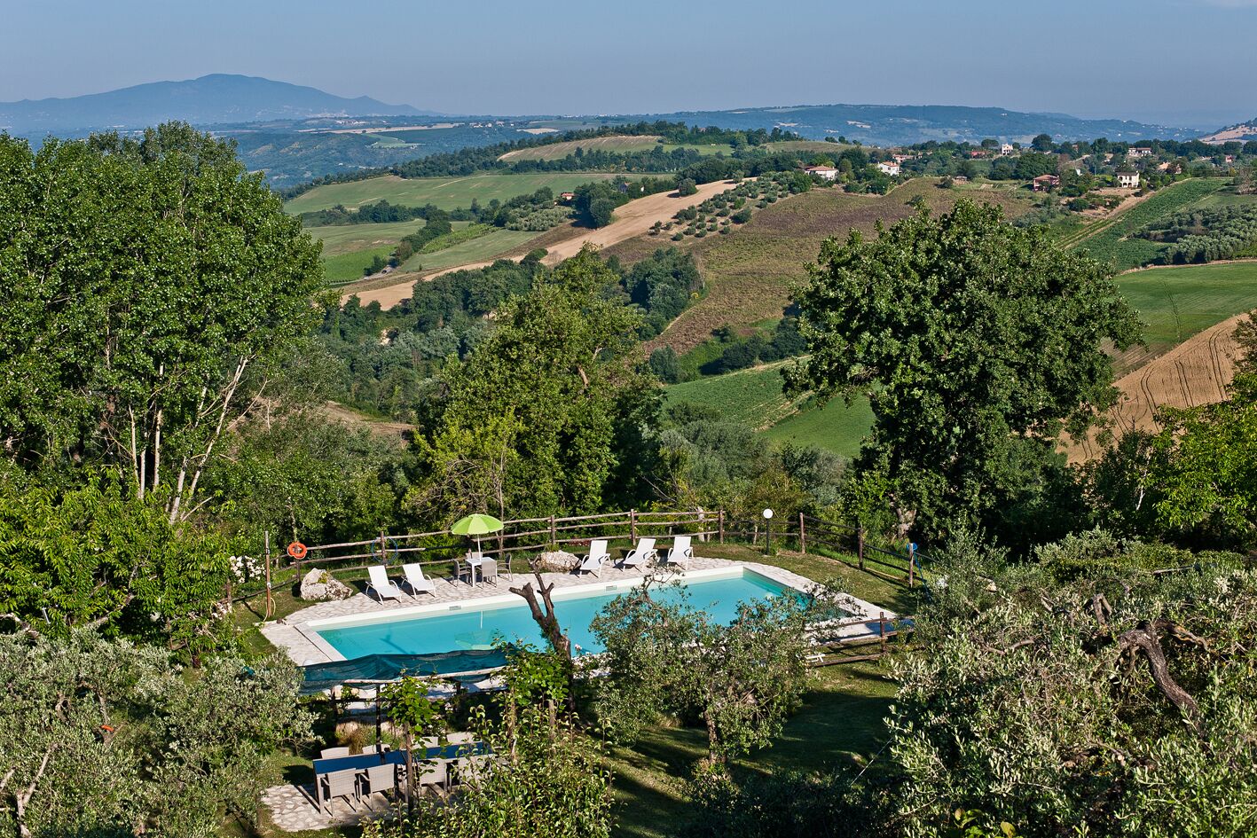 Area piscina con lettini e vista su dolci colline e montagne in lontananza.