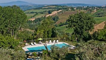Area piscina con lettini e vista su dolci colline e montagne in lontananza.