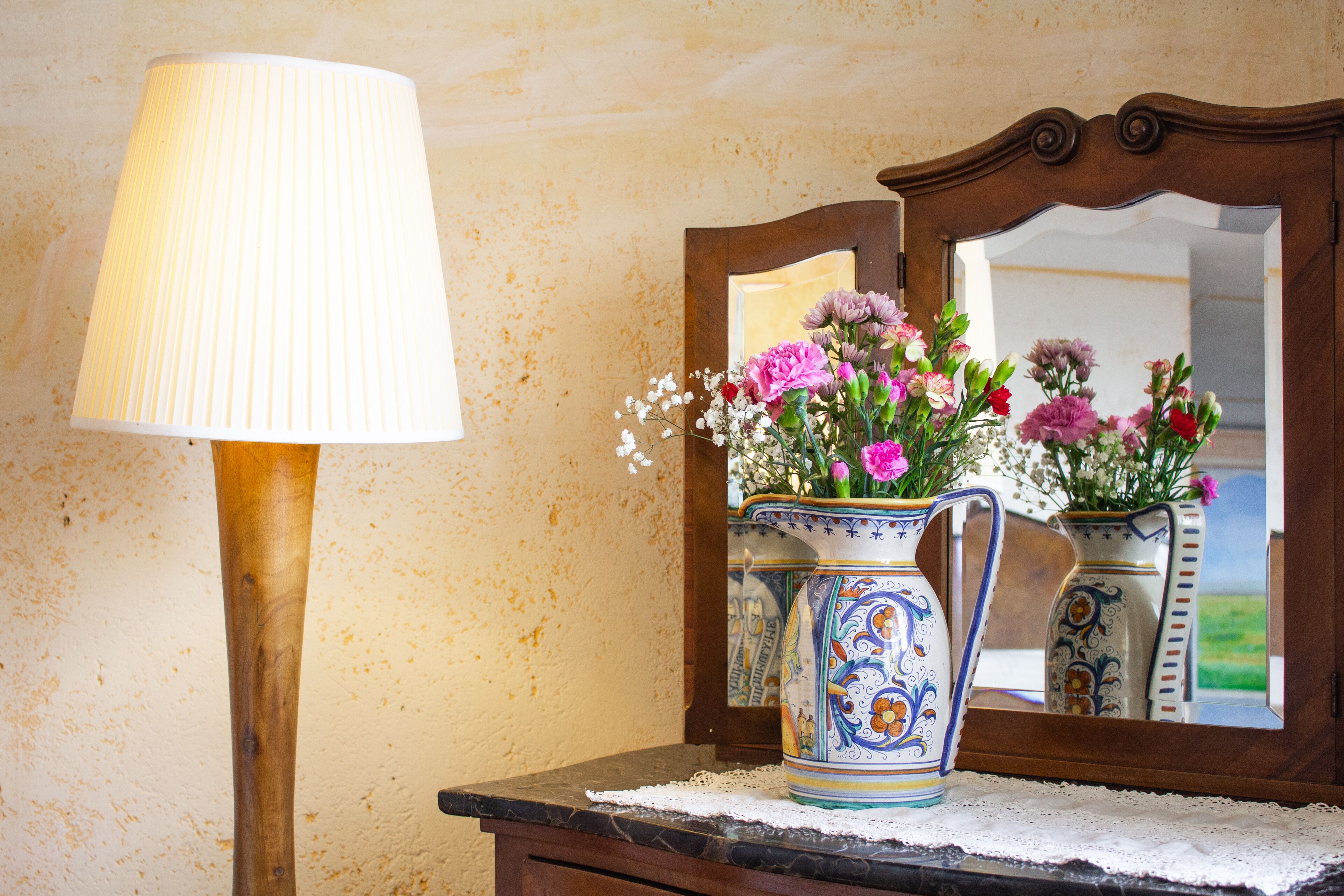 Um candeeiro, um vaso com flores e um espelho sobre uma mesa.