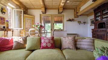 A cozy living room with a green sofa, a wooden ceiling, and a window with a view of greenery.