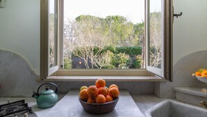 Une cuisine avec une fenêtre, un saladier rempli d’oranges et une bouilloire.