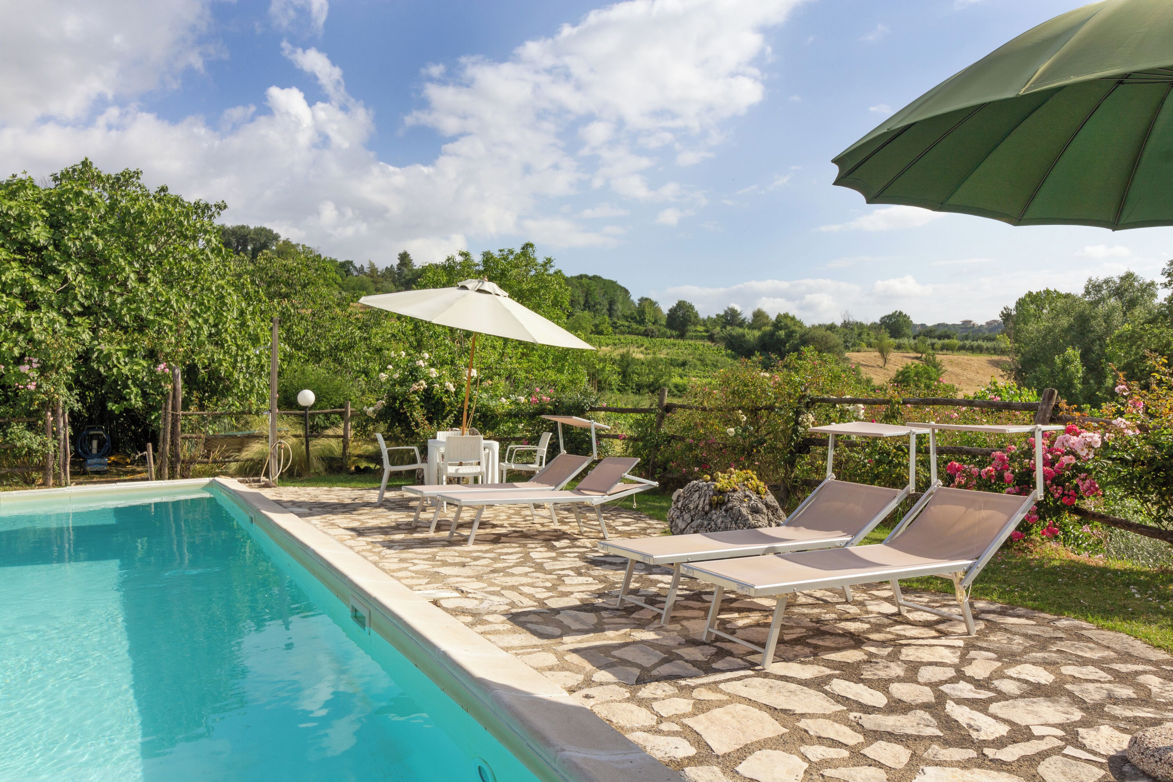 Ein Poolbereich mit Steinböden, Liegestühlen und Sonnenschirmen.