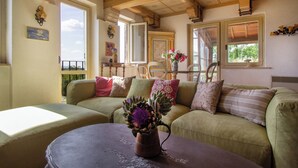 Un salon chaleureux avec un canapé vert, une table basse ornée d’un vase de fleurs et un plafond en bois.
