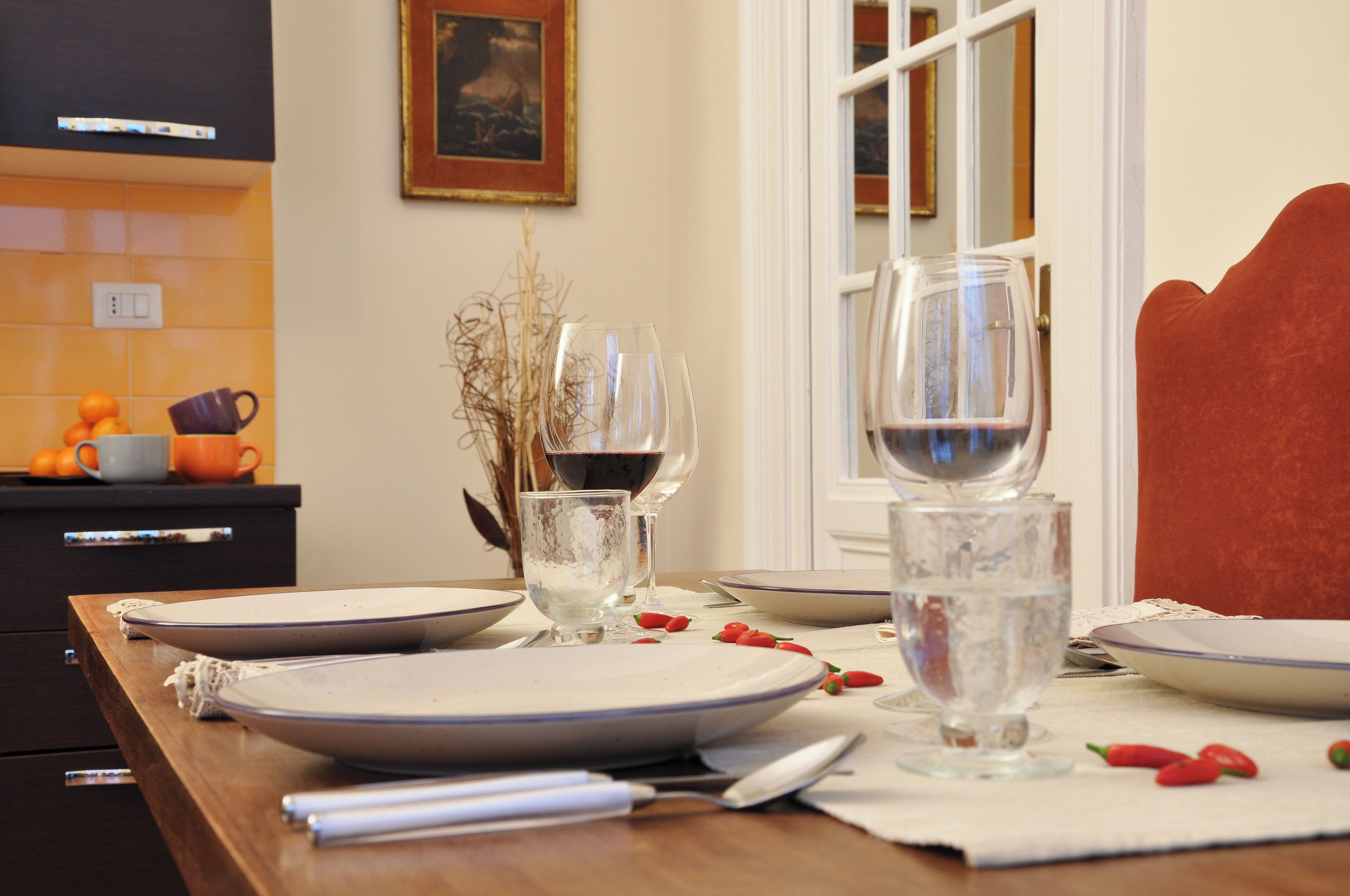 A dining table set with plates, glasses, and cutlery, with a window and a painting in the background.
