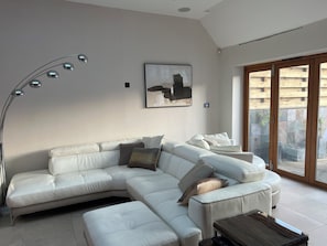 A modern living room with a sectional sofa, a floor lamp, a painting, and a sliding glass door leading to an outdoor area.