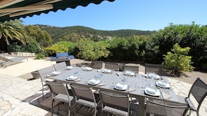 An outdoor dining area with a table set for six, surrounded by chairs, and a grill in the background.