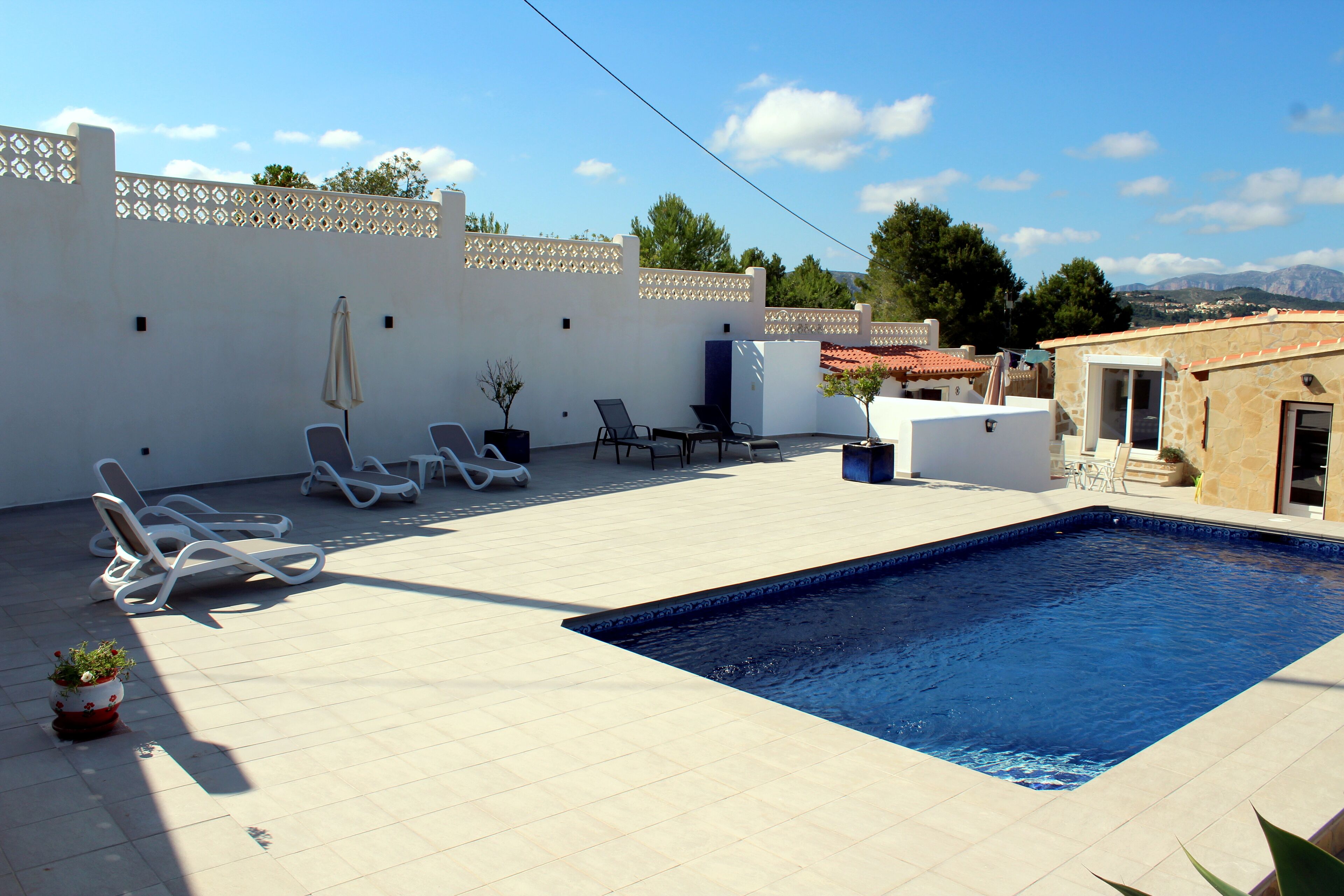 A swimming pool with lounge chairs and a small table, surrounded by a white wall with decorative lattice.