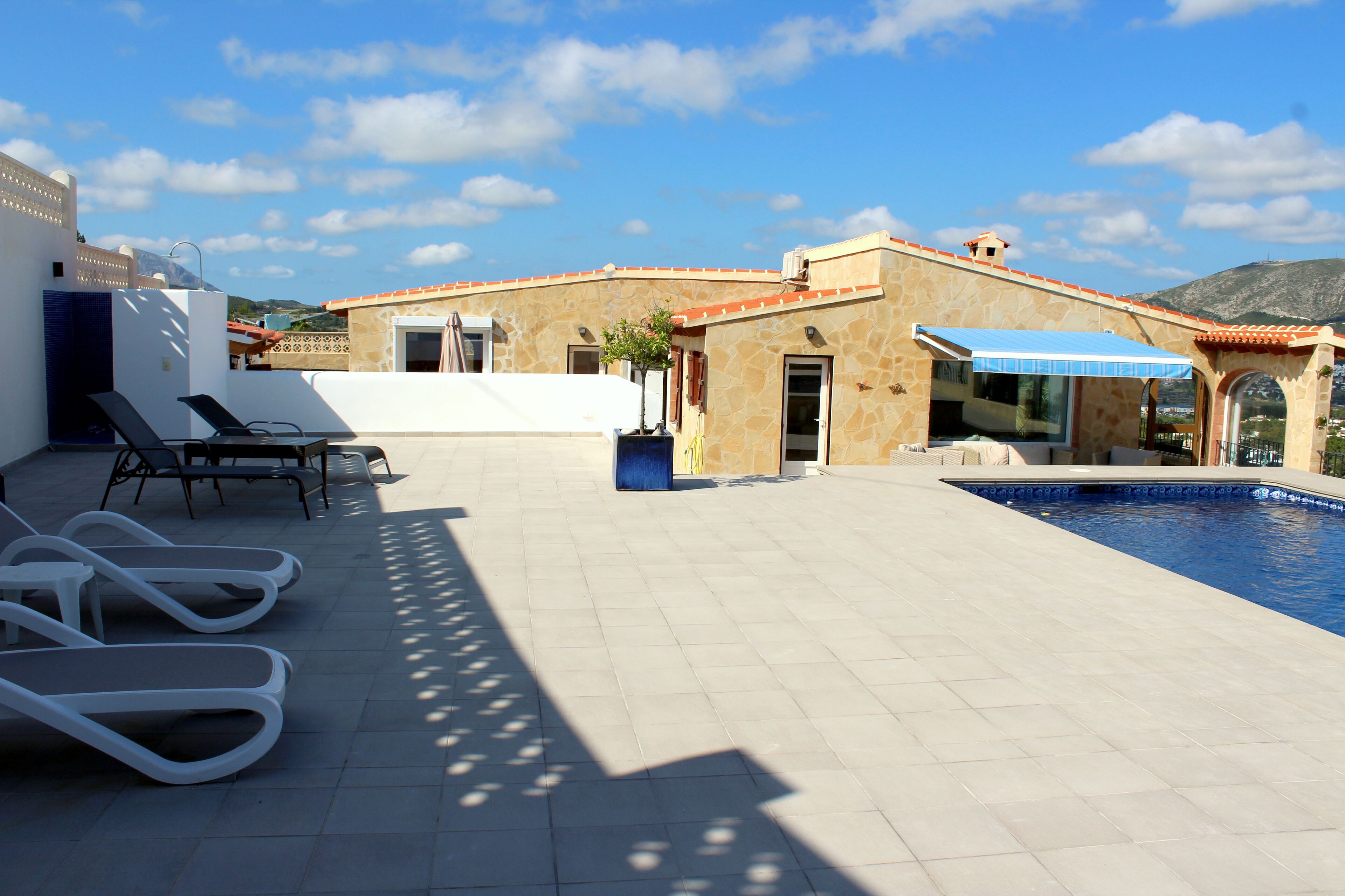 Uma área de piscina no terraço, com espreguiçadeiras, piscina e um edifício com telhado de azulejos.