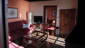 Een woonkamer met een rode bank, een glazen salontafel, een flatscreen televisie en een houten deur.