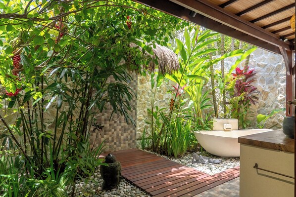 Ein Garten mit einer Holzterrasse, einer Steinmauer und verschiedenen tropischen Pflanzen.