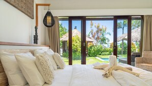 Ein Hotelzimmer mit einem großen Bett, Blick auf Pool und tropischen Garten sowie einer Reetdachkonstruktion im Außenbereich.